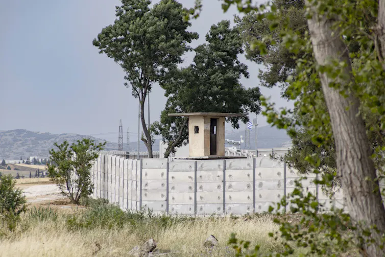 A nearly ten foot high concrete wall is shown with a guard tower.