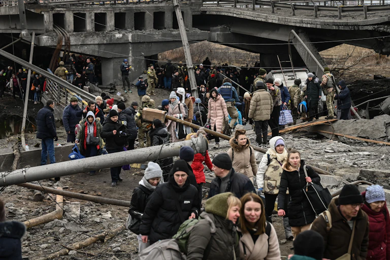 People dressed in winter coats and hats are seen walking pass ruins of a bridge destroyed during Russian invasion.