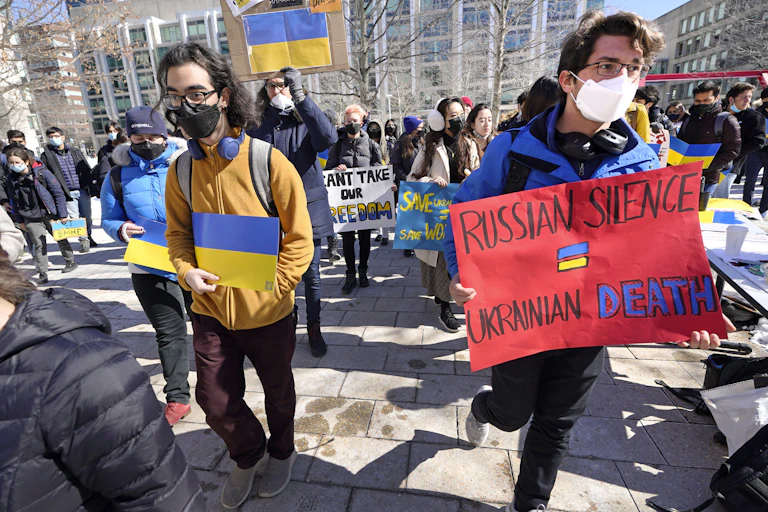 People seen at a protest carrying paper Ukrainian flags and a sign 'Russian silence = Ukrainian death