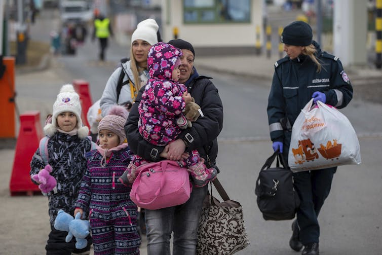 Women and children walk down the street, carrying bags