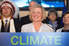 A blonde woman smiles behind a podium that says 'climate.'