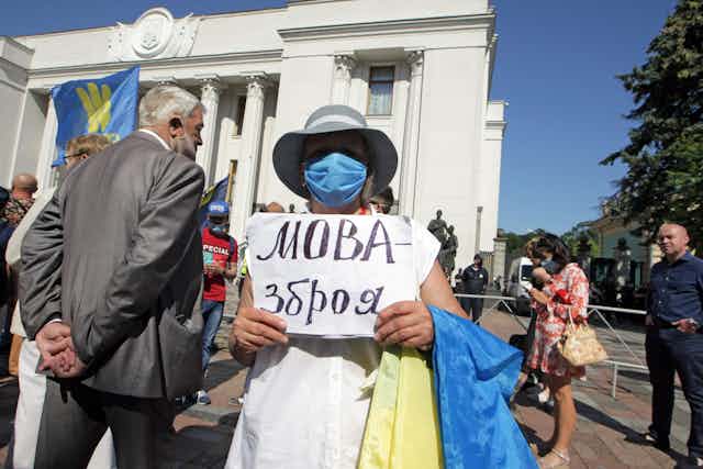 Woman wearing a blue face mask holds a sign as she stands in front of a columned public building.