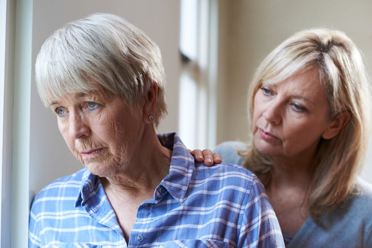 Older woman looks concerned with supportive younger woman standing behind her