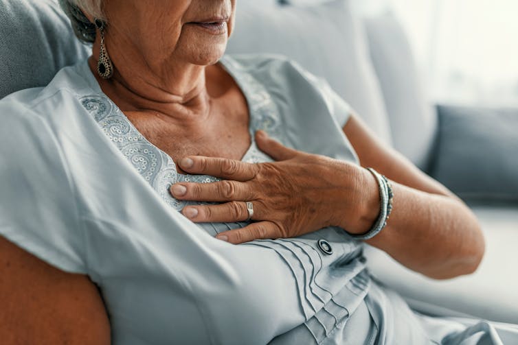 Older woman sitting in a chair puts a hand to her chest.