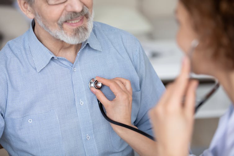 Doctor listens to man's chest with stethoscope.