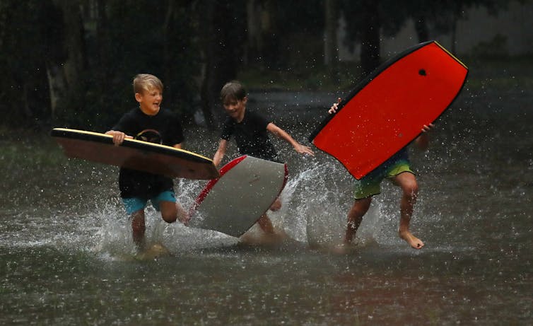 three boys in wetsuits and boogie boards play in water
