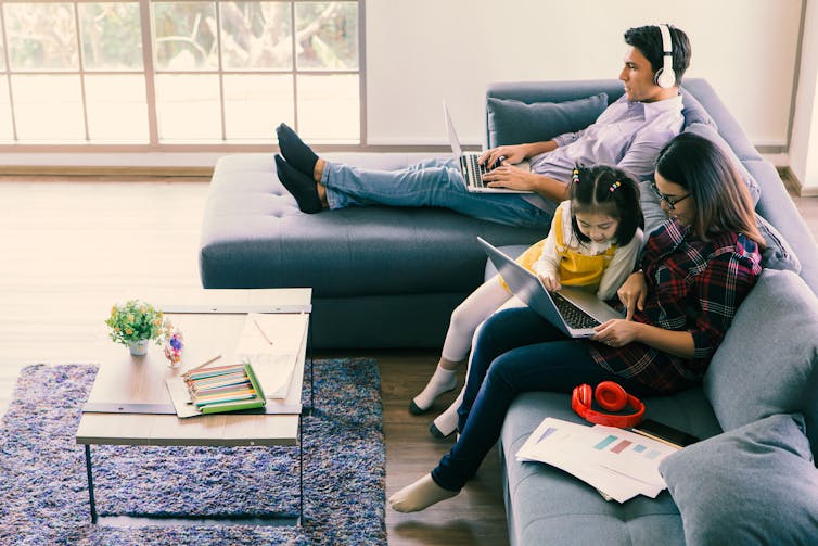 El niño exige la atención de la madre, mientras que el padre se sienta a un lado trabajando con auriculares.