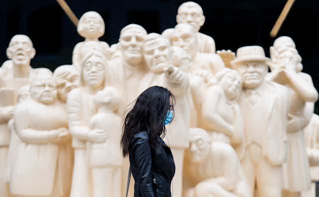 A woman wearing a black leather jacket walks by a white sculpture of a crowd of people