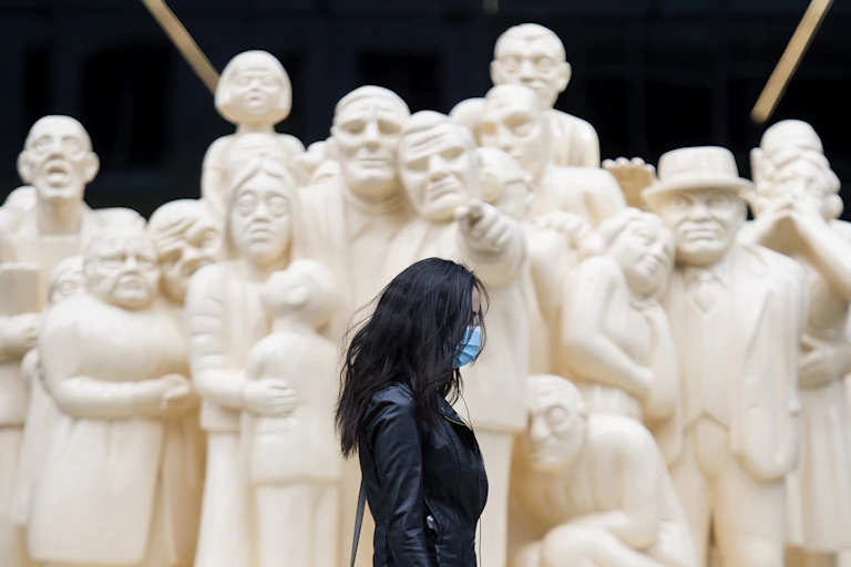 A woman wearing a black leather jacket walks by a white sculpture of a crowd of people