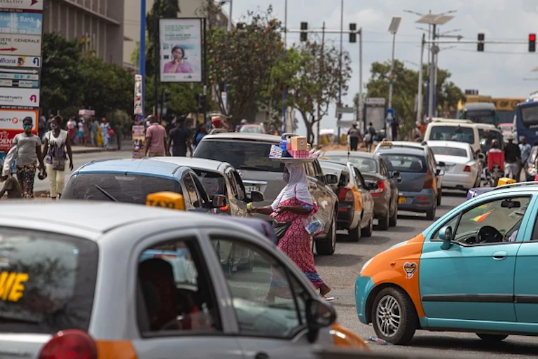People walk through traffic in Accra