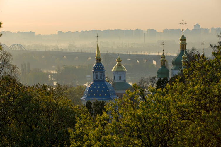 The painted spires of an Orthodox Church seen at sunrise with a cityscape in the background.