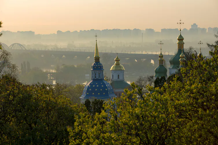 The painted spires of an Orthodox Church seen at sunrise with a cityscape in the background.