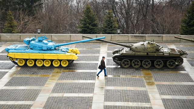 A man walks past a memorial made up of two tanks, one painted in Ukraine's national colors of blue and yellow