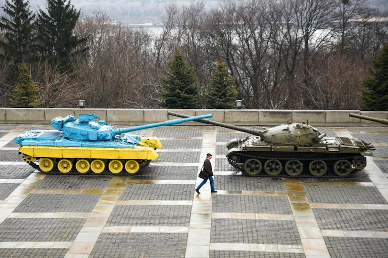 A man walks past a memorial made up of two tanks, one painted in Ukraine's national colors of blue and yellow