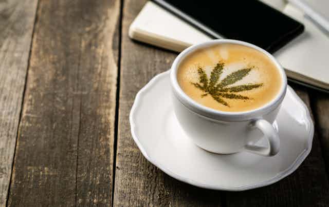 A cup of coffee with a marijuana leaf stenciled on top