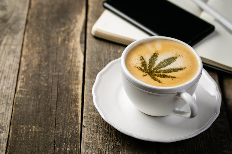 A cup of coffee with a marijuana leaf stenciled on top