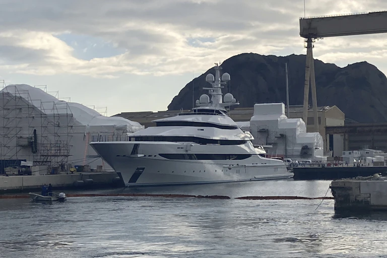 A large gleaming white yacht sits in a harbour.