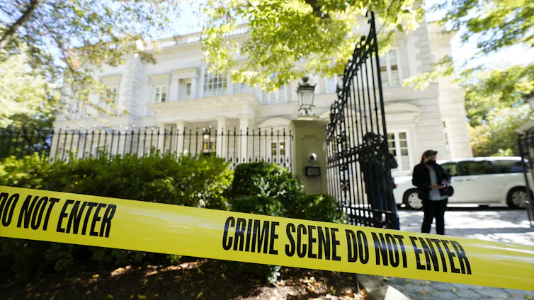 yellow police crime scene tape and federal agents are seen outside an elegant white stone mansion framed by leafy trees