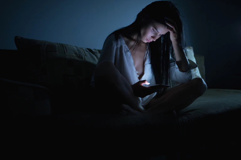 femme qui regarde son téléphone cellulaire en tenant sa tête avec ses mains