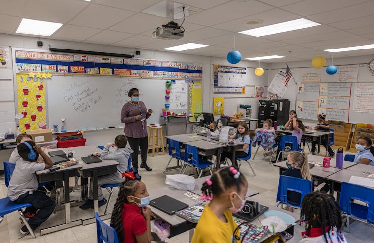 An adult stands in the front of a classroom with young children at desks