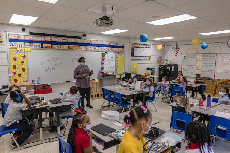 An adult stands in the front of a classroom with young children at desks