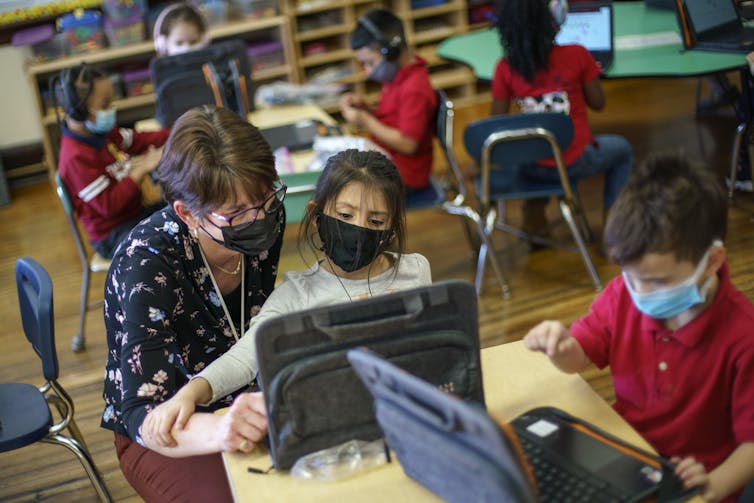 An adult approaches a young person in a school classroom