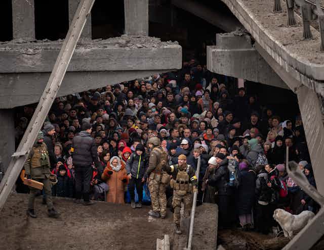 A crowd of people gather under a destroyed bridge.
