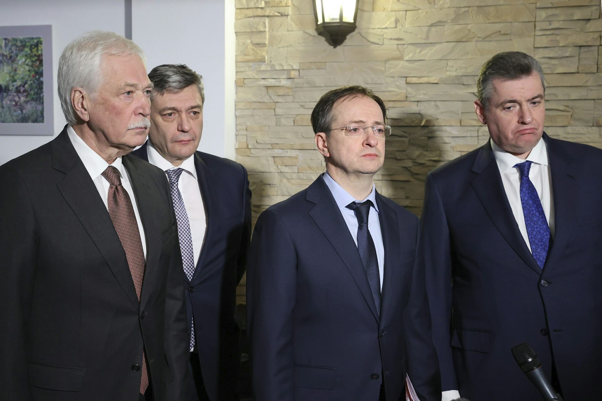 Four men in dark suits stand beside each other.