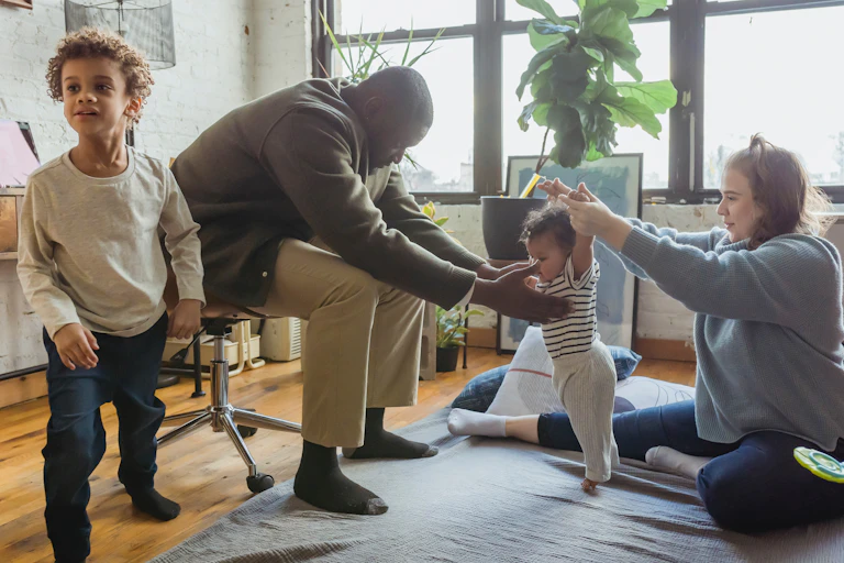 A child seen lunging / stretching while two parents attend to a baby lerarning to stand.