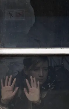 A young girl holds her hands to the glass of a train car.
