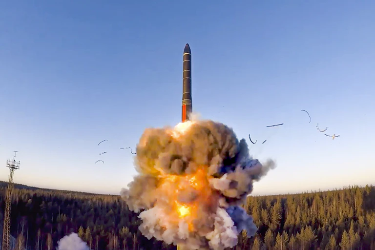 a ball of fire and smoke beneath a missile rising into a cloudless blue sky above a forest