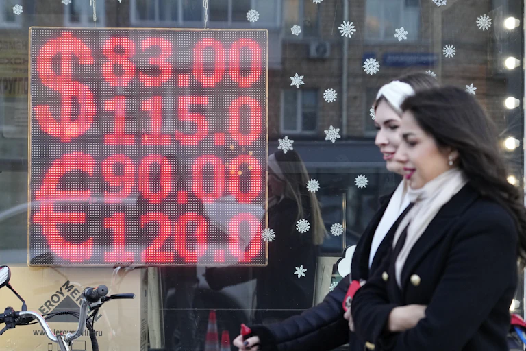 Two women walk in front of a screen displaying the exchange rates of U.S. Dollar and Euro to Russian Rubles