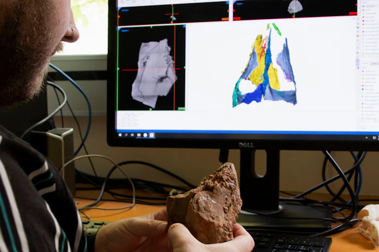 Tim Frauenfelder holding the Boulia ankylosaur skull, with 3D models in the background