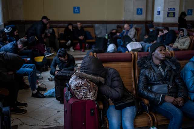 Dozens of refugees wait on the floor and benches at a railway station.