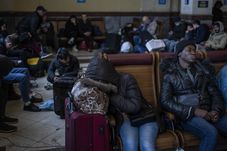 Dozens of refugees wait on the floor and benches at a railway station.