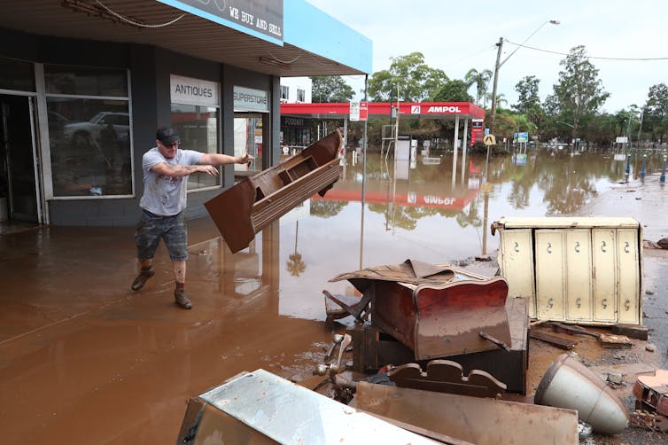 man thrown furniture onto pile amid floodwaters