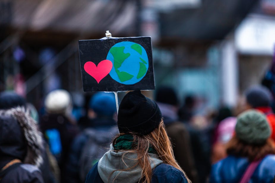 A person carries a picket sign with an illustration of the Earth and a heart.
