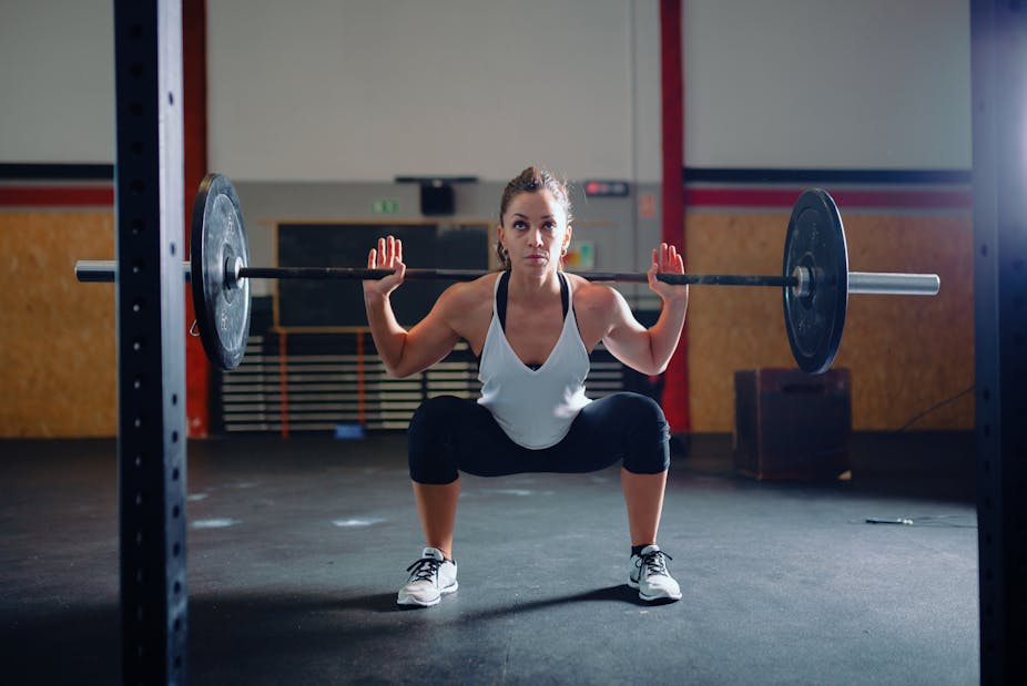 A young woman performs a barbell squat in the gym.