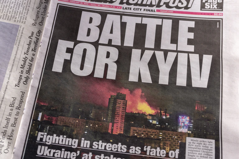 "BATTLE FOR KYIV" blares a page one newspaper headline, with a photo of burning buildings in Kyiv.