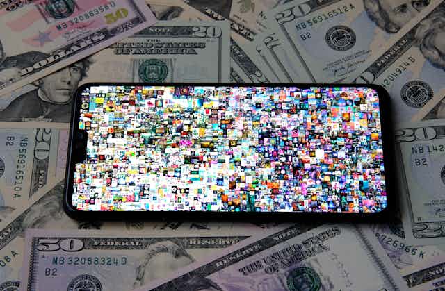 Photo of a mobile phone with Beeple's Everydays artwork on screen, a collage of dozens of tiny photos. The phone is sitting on a pile of US 50 and 20 dollar bills.