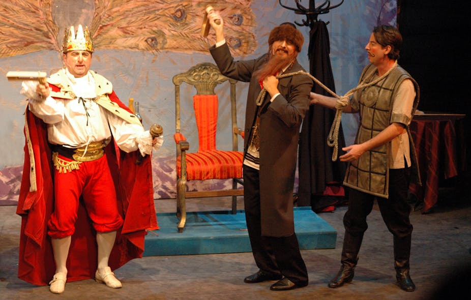Three actors on stage, with one dressed as a king wearing a crown and a cape, and another dressed as a rabbi, with a long beard.