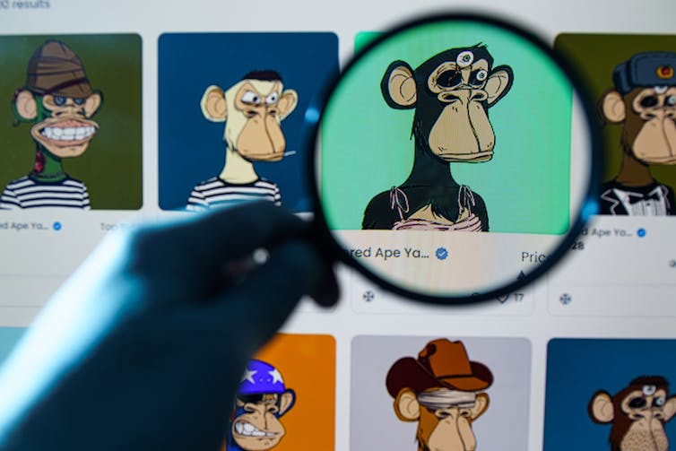 A hand holds a magnifying glass up to a screen showing several NFTs from the Bored Ape Yacht Club.