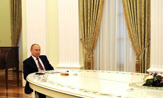 Vladimir Putin sits alone at his negotiating table in the Kremlin.