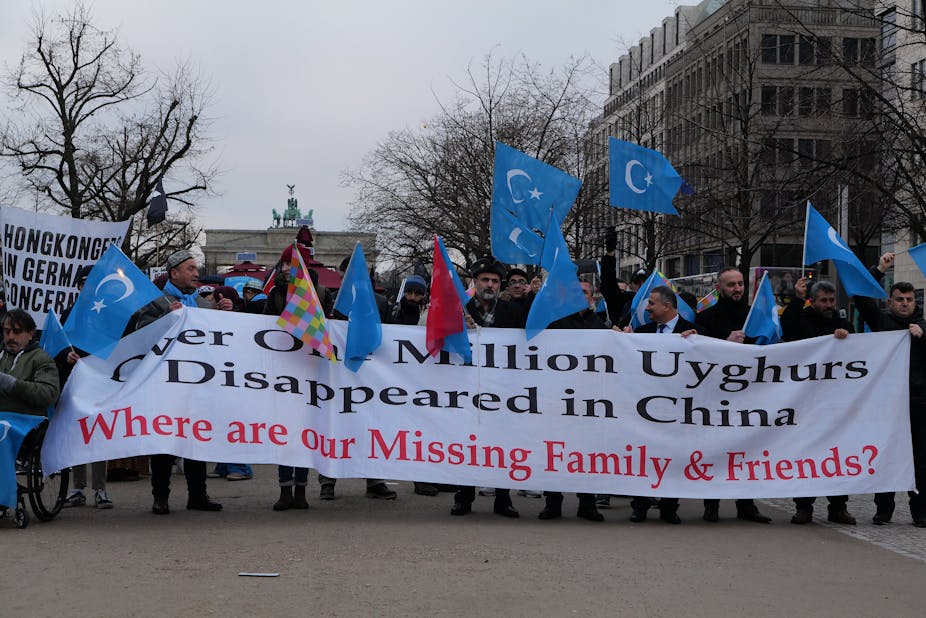 People with flags march carrying a banner reading over 1 million Uyghurs disappeared in China -- where are our missing family and friends?