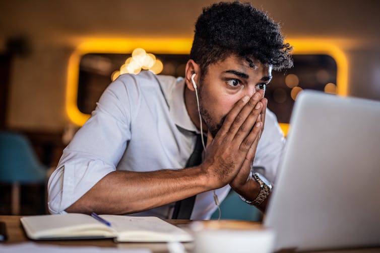 A worried-looking man at a desk, looking at his computer screen.