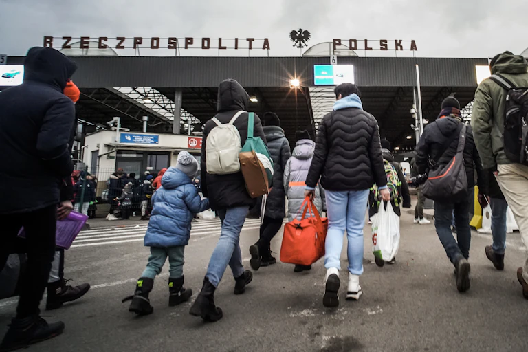 The backs of people carrying bags are shown as they march towards the Poland border