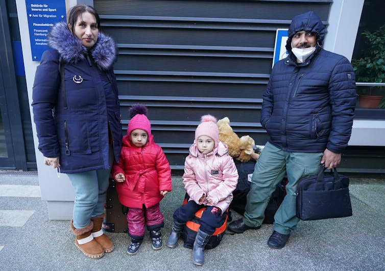 A woman in a dark coat poses with two young girls, also in winter clothing, and a man next to them.