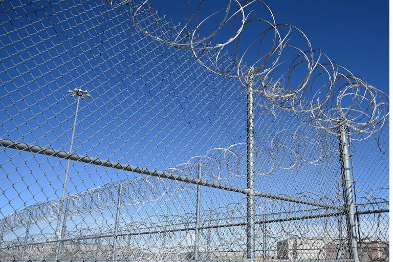 The corner of a chain-link fence with barbed wire on top of it.