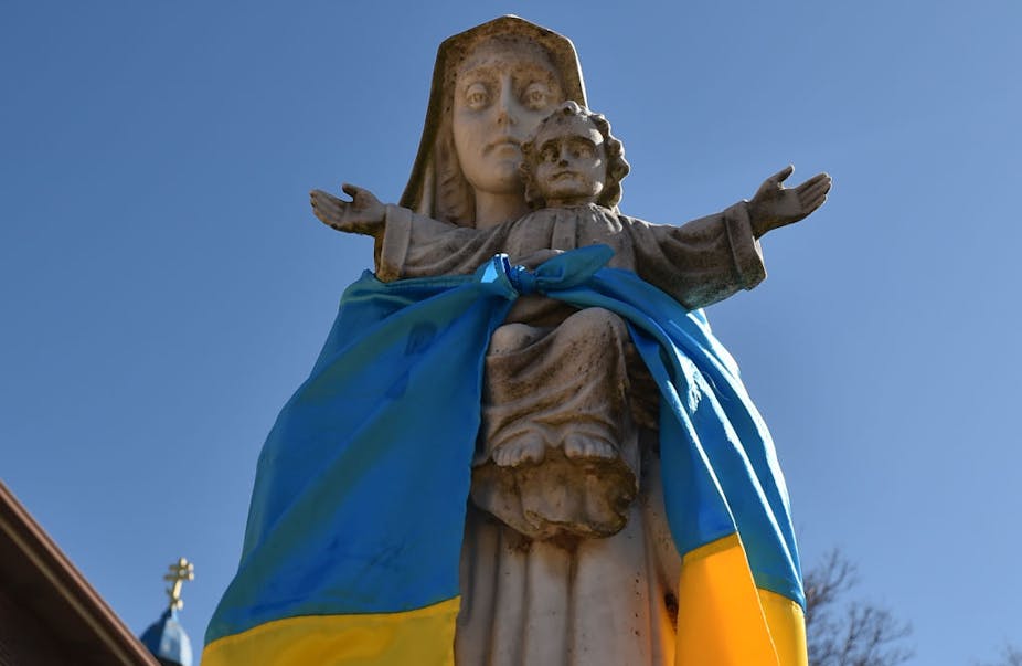 A blue and yellow flag draped around a statue of a woman and child.