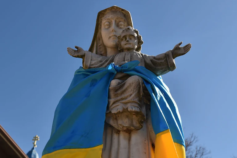 A blue and yellow flag draped around a statue of a woman and child.